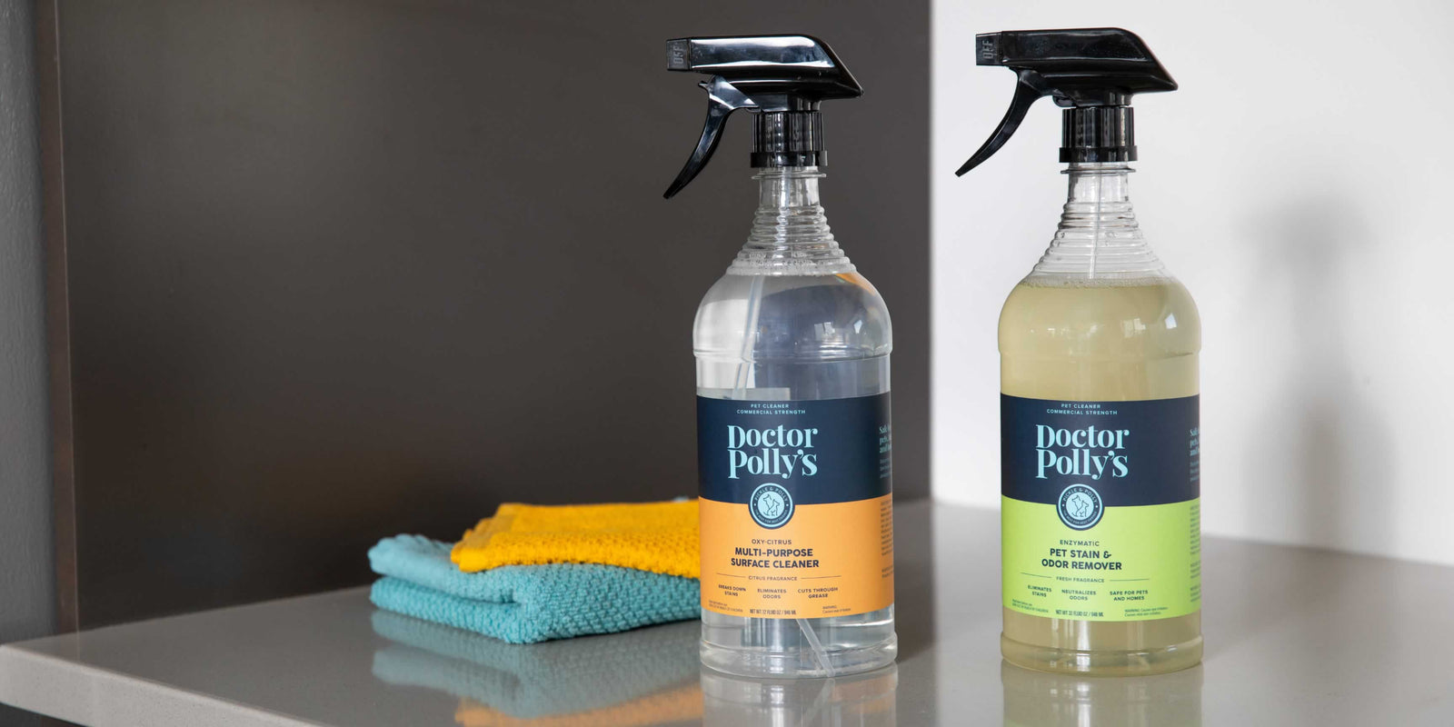A bottle of Dr. Polly' All Purpose Oxy Cleaner and Dr. Polly's Stain & Odor Remover on a table next to cleaning rags.